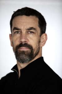 Colin Murphy 2026 headshot. Colin is photographed in front of a white background. He is wearing a black jumper and has dark hair and a beard.