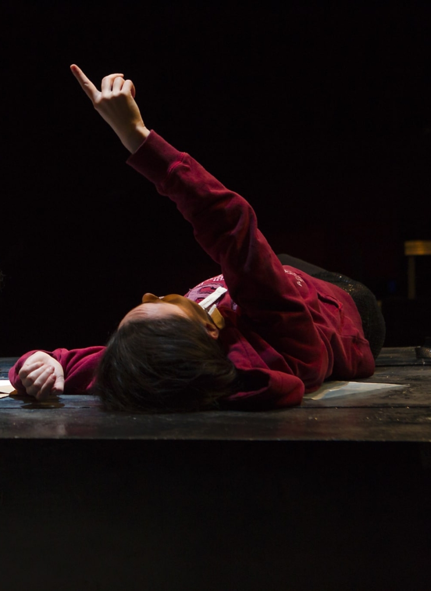 Two teenage girls lie on the ground drinking a bottle of cider and pointing at the sky.