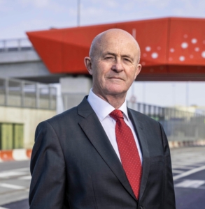 Photo of Eamonn O Reilly, board member, standing on the road at Dublin Port, wearing a dark grey suit, white shirt and red tie.